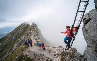 Personen auf Wanderweg, die zu einer Wanderin an einer Leiter schauen