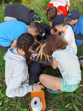Kinder lehnen über einer Feuerschale und bereiten ein Lagerfeuer vor.