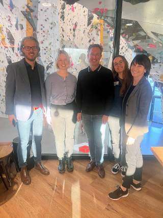 5 Menschen stehen nebeneinander vor einer Kletterwand