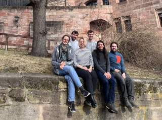 Sechs junge Menschen sitzen auf Mauer vor altem Backsteingebäude