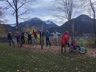 Menschen balancieren zusammen auf einem Seil und halten sich an den Händen. Eine Person im Rollstuhl gibt der Gruppe Stabilität.