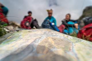 Wanderkarte im Vordergrund, verschwommen im Hintergrund sitzende Gruppe von jungen Menschen.