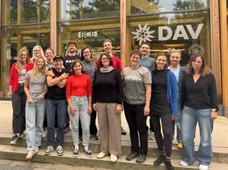 15 Personen vor einem Bürogebäude mit DAV-Logo