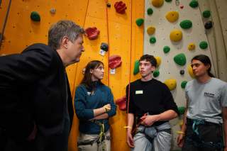 Drei junge Menschen mit Klettergurt im Gespräch mit Robert Habeck vor einer Kletterwand