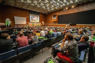 Ein großer Saal voll mit Leuten und einer Bühne