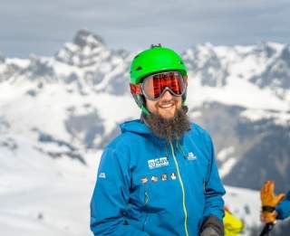 Ein Mann in voller Schneeausrüstung steht in den schneebedeckten Bergen und lacht in die Kamera