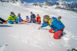 Einer Gruppe Kindern wird im Schnee wichtiges über Lawinen erklärt