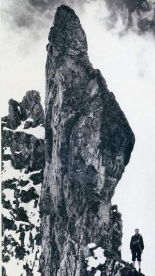 Ein hoher, einsamer Berggipfel; klein in der Ecke ist ein Kletterer zu sehen