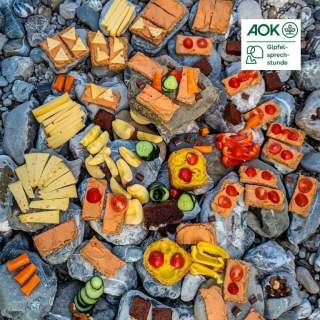 Ein Bild von einem Buffet auf einer Kiesbank mit verschiedensten belegten Broten, Obst und Gemüse