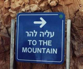 Ein Schild direkt vor einem Felsen. Das Schild ist zweisprachig beschriftet
