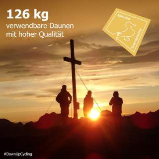 Drei Personen stehen am Gipfelkreuz und schauen in den Sonnenauf/-untergang