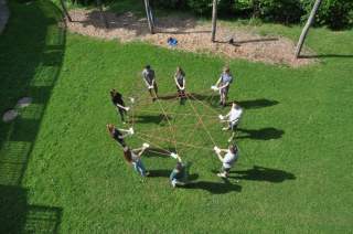 Eine Gruppe spielt mit Seilen auf einer Wiese; sie werden von oben fotografiert