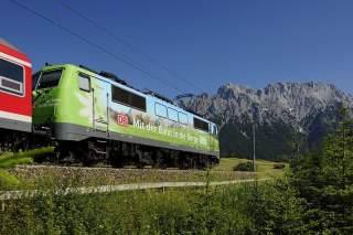 Eine Lock der Deutschen Bahn fährt in Richtung der Berge; Im Hintergrund ist eine Bergkette zu sehen