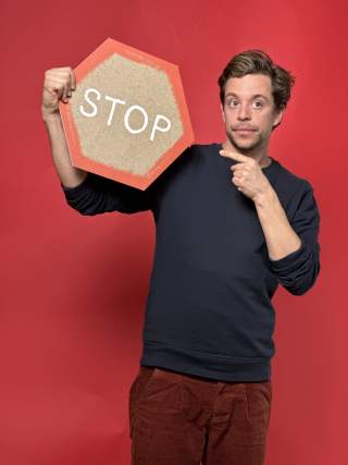 Ein Mann steht vor einem roten Hintergrund und zeigt auf ein Stop-Schild, das er in der Hand hält