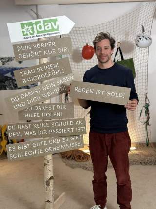Tobi Krell steht neben einem Baumstamm an dem die wichtigsten Aussagen auf Schilder