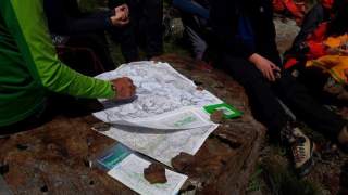 Eine Gruppe sitzt zusammen an einem Stein, in der Mitte liegt eine ausgefaltete Wanderkarte