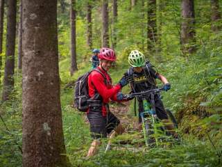 Ein Trainer hilf einem Schüler dabei einen Mountainbiketrail zu fahren