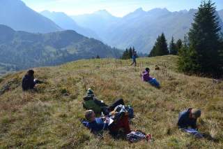 Eine Gruppe von Menschen sitzt verteilt auf einer Bergwiese