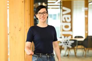 Frau mit schwarzer Bobfrisur, schwarzer Brille und schwarzem T-Shirt lehnt an einem Geländer. Frau mit schwarzer Bobfrisur, schwarzer Brille und schwarzem T-Shirt lehnt an einem Geländer.